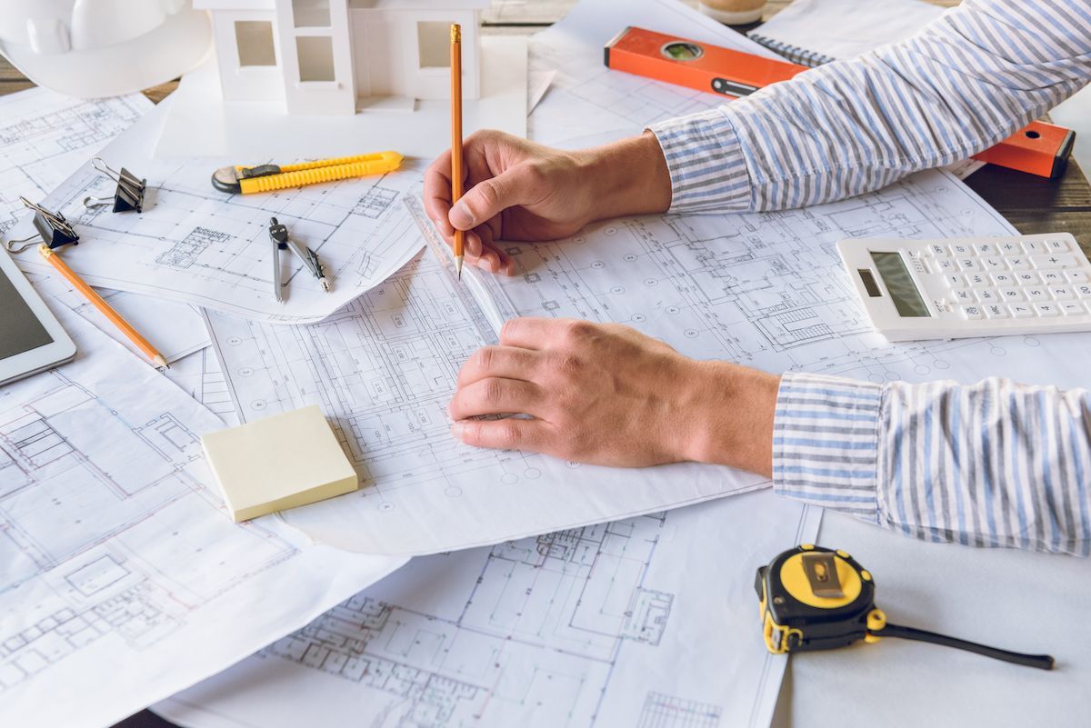 Hands sketching on architectural plans with tools and calculator on a desk