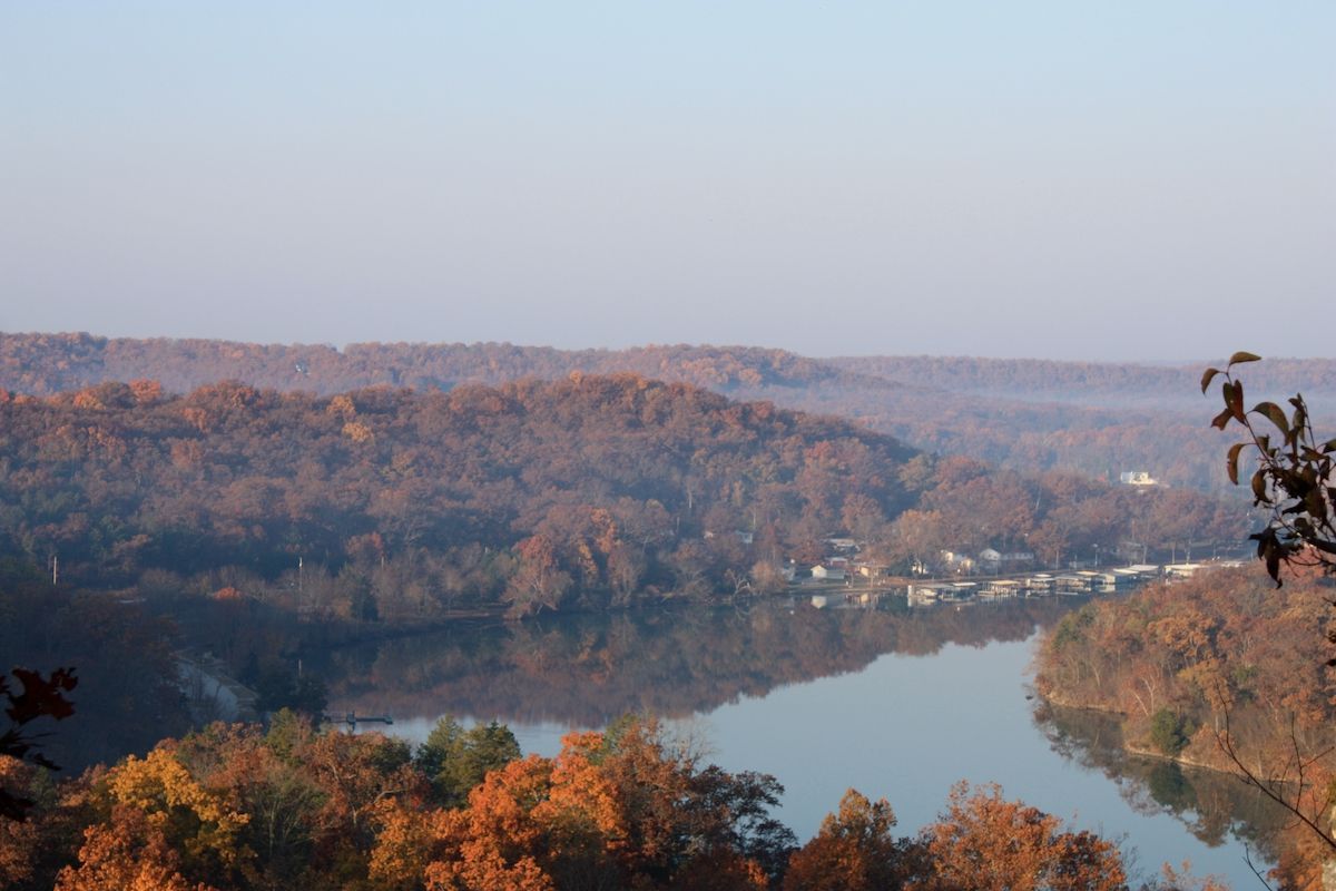 Autumn forested hills around a calm river or lake under a hazy sky