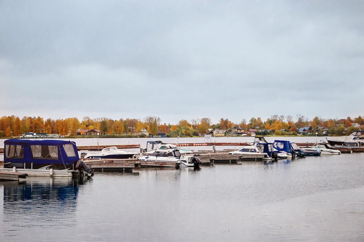Boats moored on a calm waterfront under a gray sky with autumn trees in the background