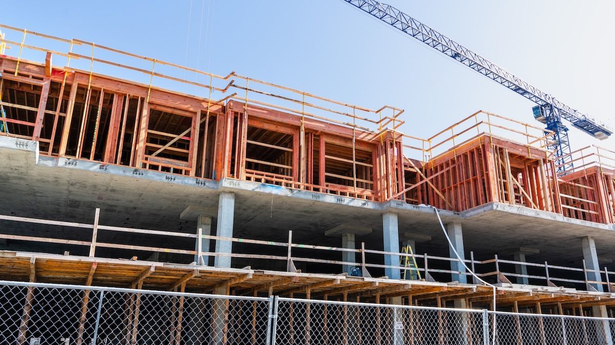 Partially built multi-story concrete building with orange framing and a crane overhead against a blue sky