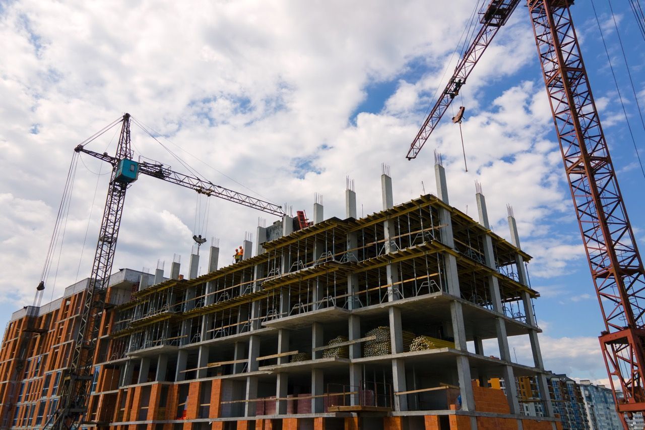Construction site with a multi-story building frame and two tall cranes against a cloudy sky