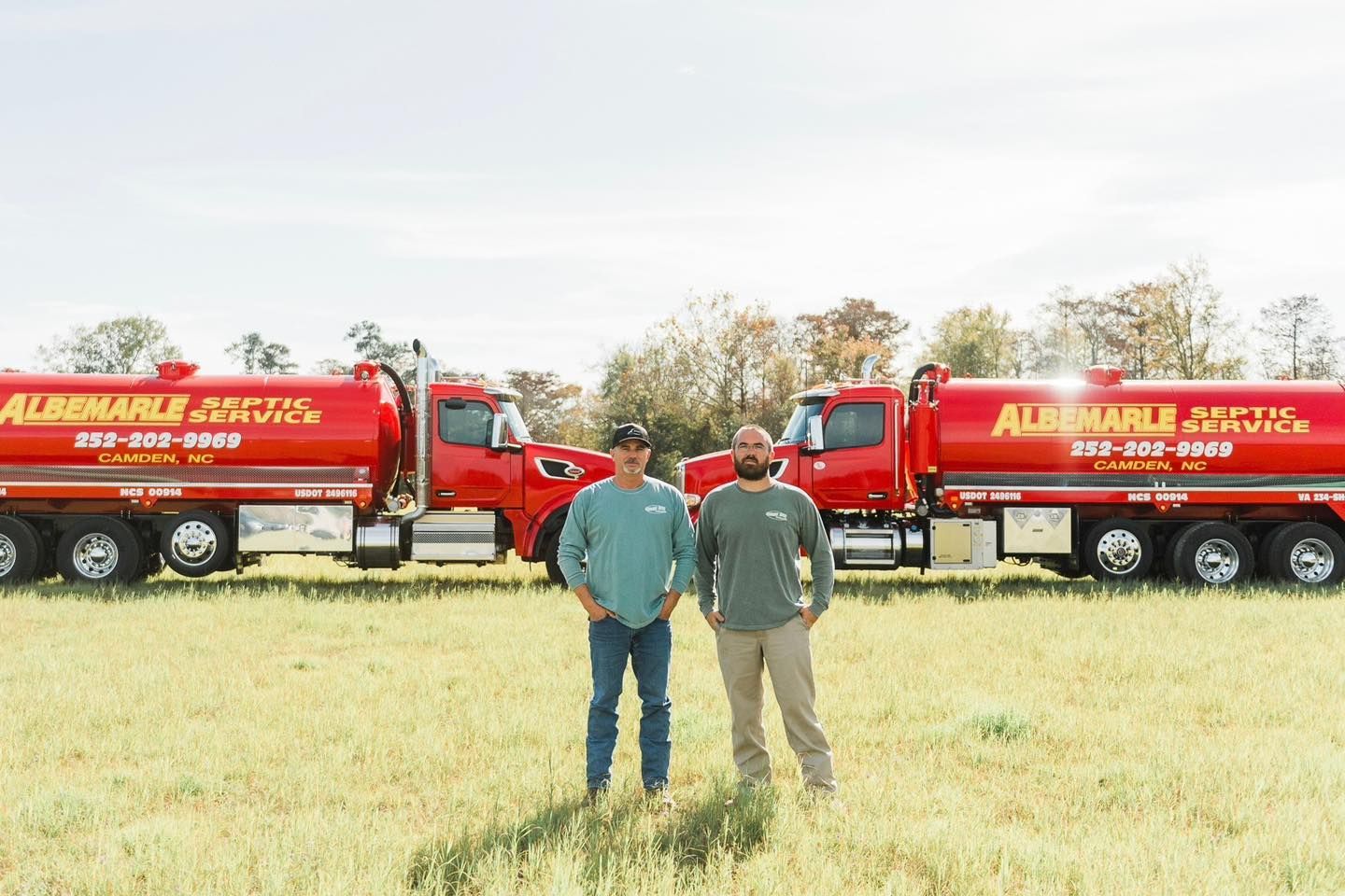 Two men are standing in a field in front of two septic tanks. Two men are standing in a field in front of two septic tanks.