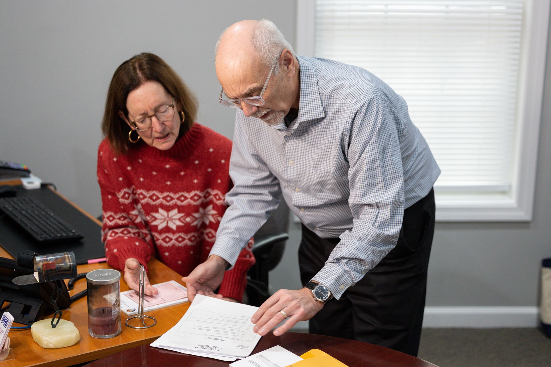 A man and a woman looking at papers on a desk in an office. The woman is wearing a red sweater.