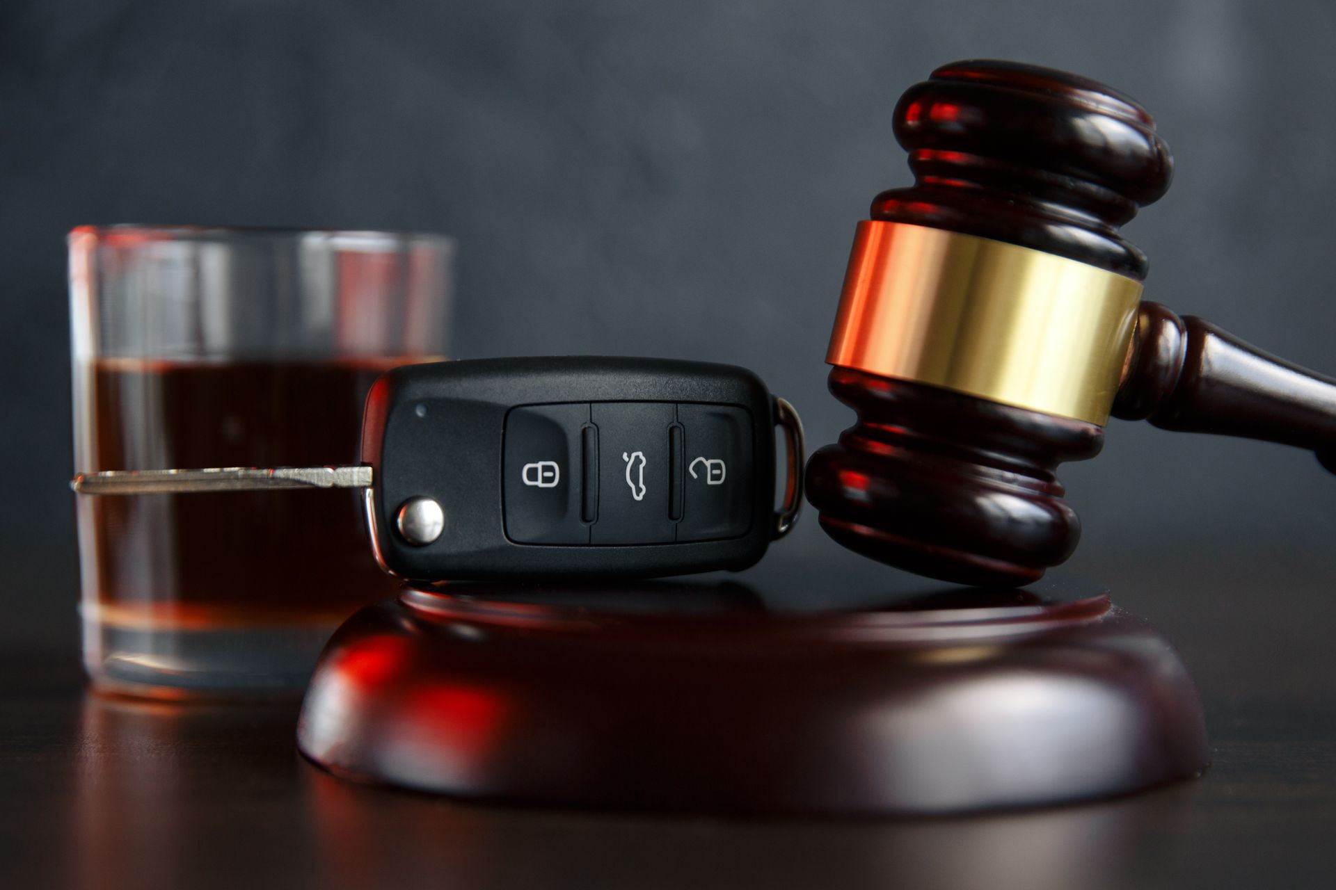 Car key and glass of whiskey beside a gavel representing a DUI attorney case.