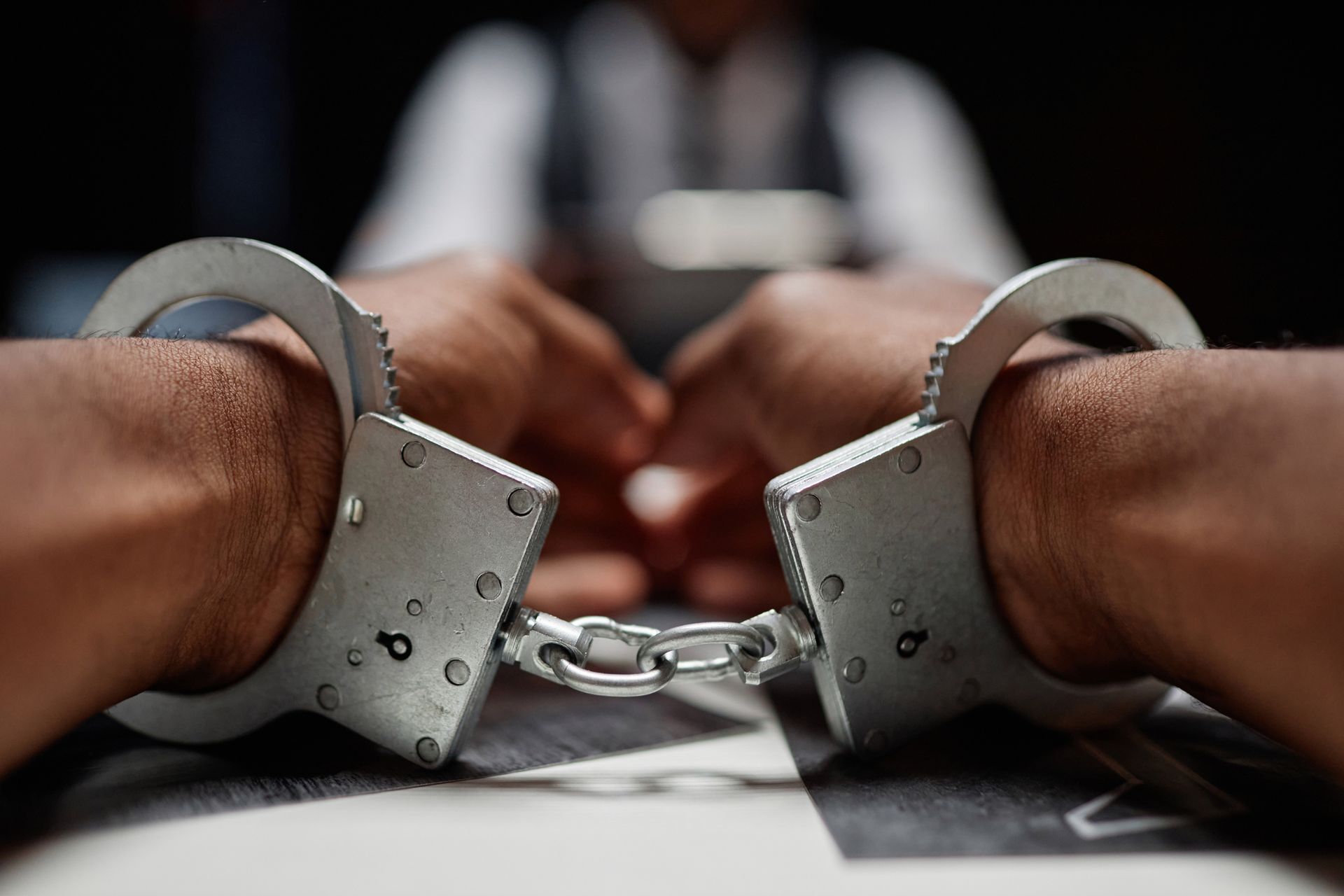 Handcuffs and gavel, with a hand reaching for handcuffs, against a white background.