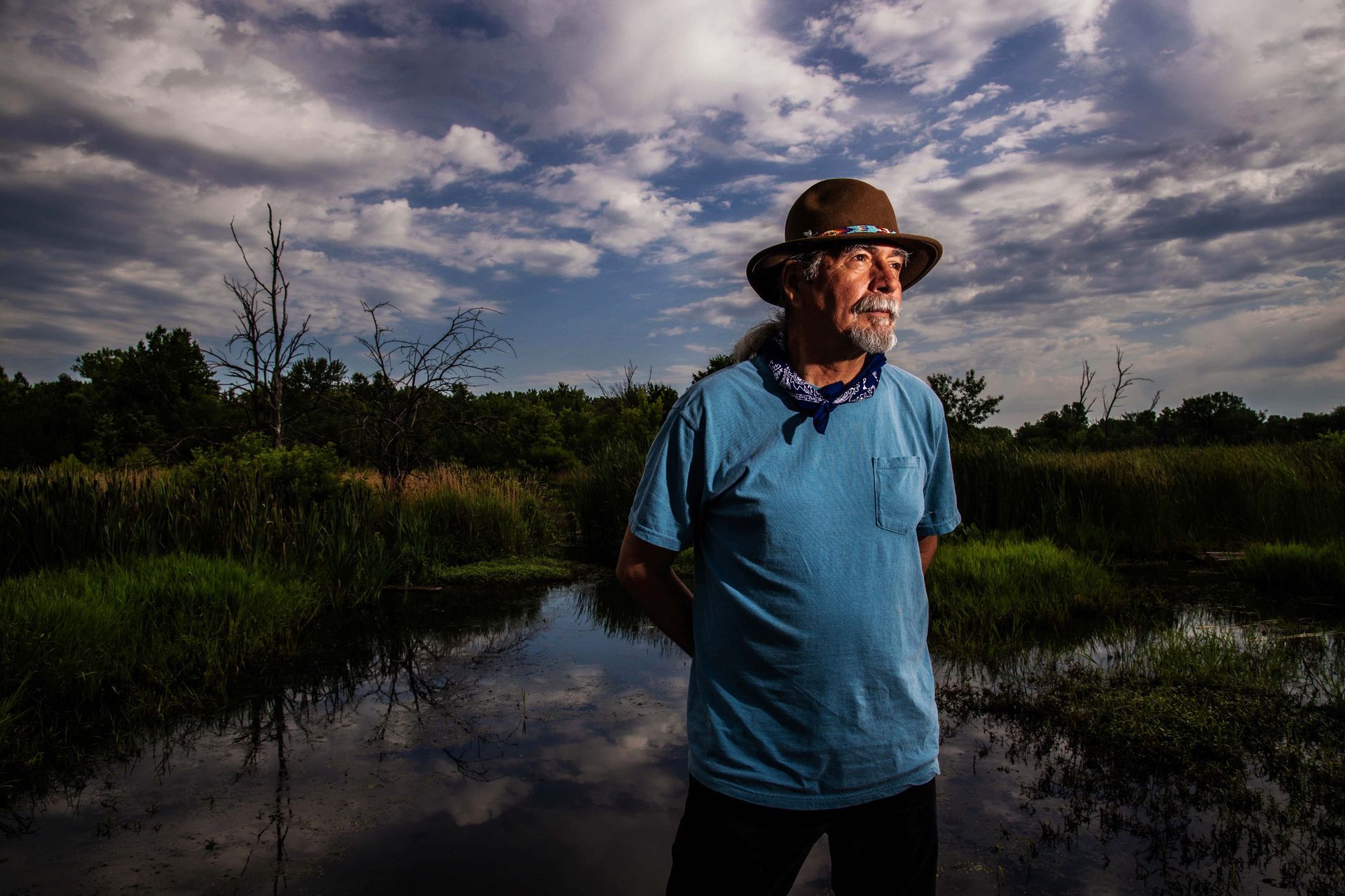A man wearing a hat and a blue shirt is standing in a muddy field.