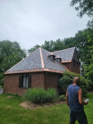 Brick house with dark roof in a wooded yard, with a man standing in the foreground.