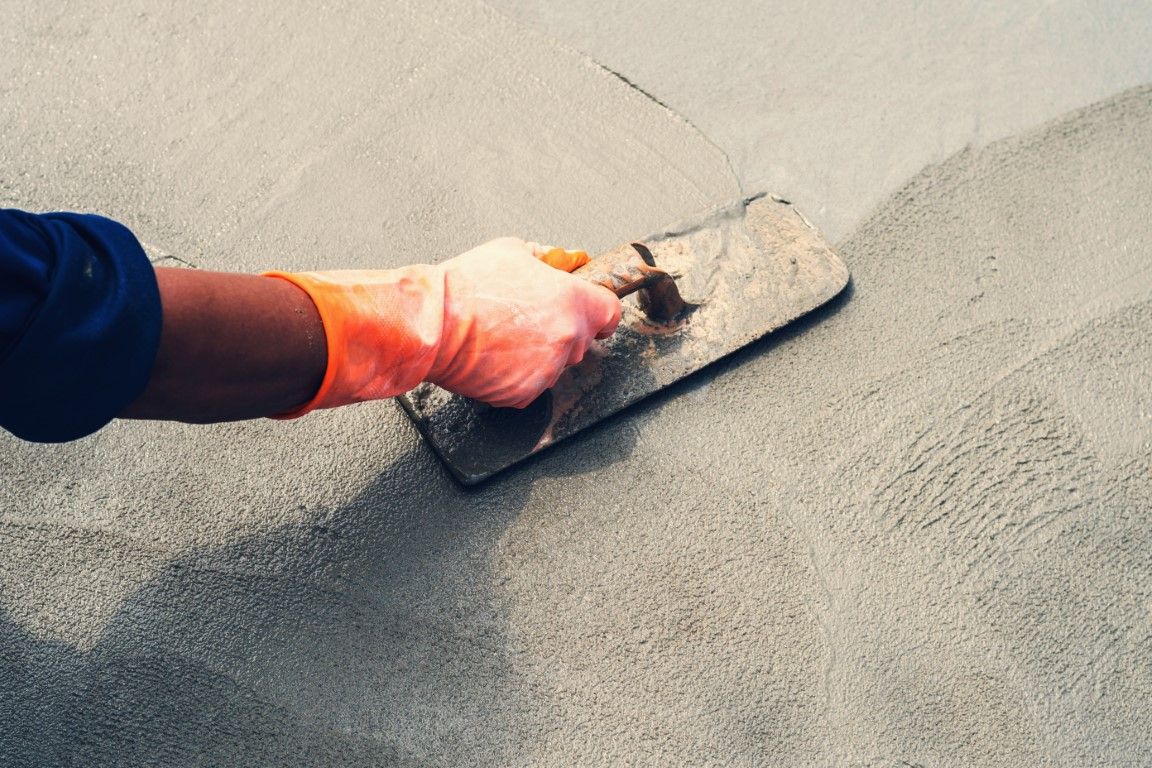 Hand with orange glove holding a trowel, smoothing concrete.