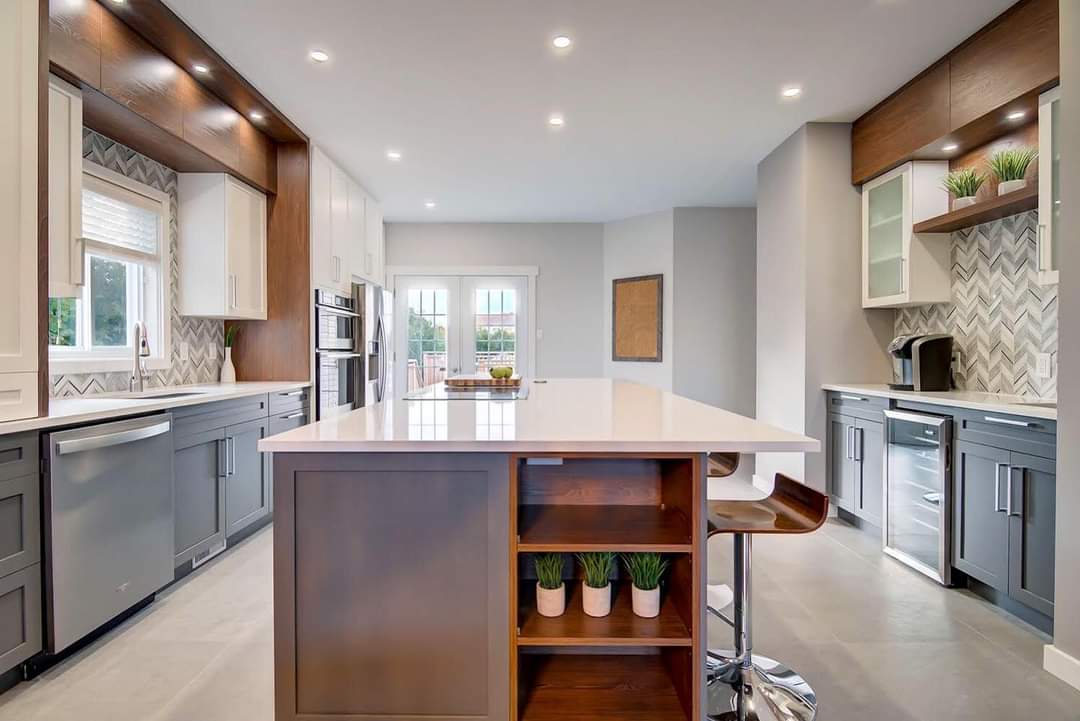 Cuisine moderne avec îlot central, armoires grises, électroménagers en acier inoxydable et éléments en bois.