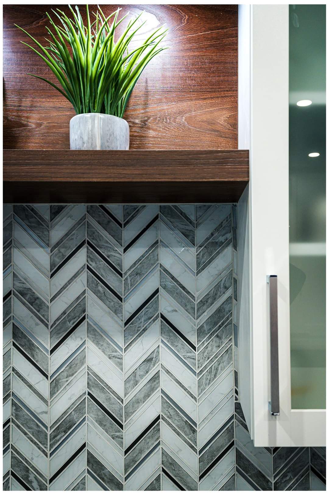 Crédence en carrelage à chevrons avec étagère en bois supportant une plante en pot. Meuble blanc à droite.