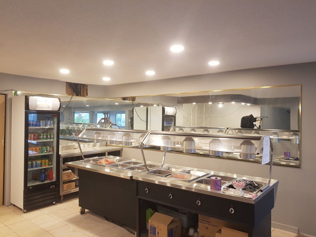 Buffet avec mur de miroirs. Comprend un réfrigérateur à boissons, des récipients alimentaires et un espace de préparation.