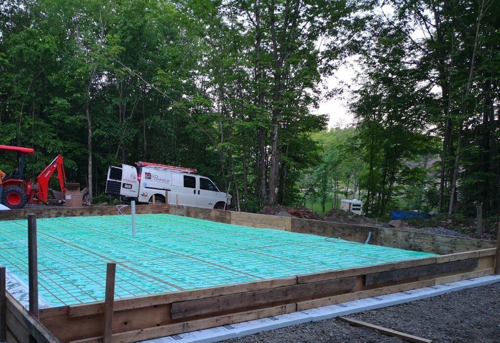 Chantier de construction avec isolation verte, ossature bois, barres d'armature et une camionnette dans une zone boisée.