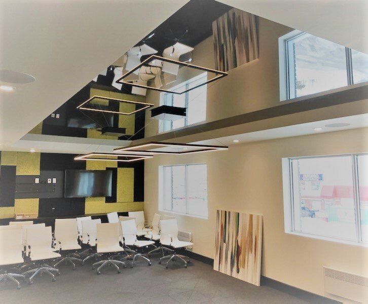 Salle de réunion avec plafond miroir, luminaires carrés modernes, chaises blanches et art abstrait.