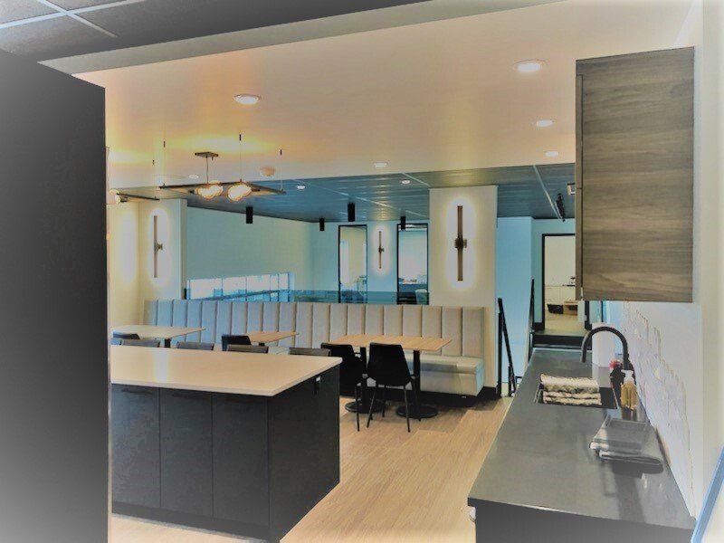 Cuisine de bureau moderne avec tables, banquettes et placards gris foncé.