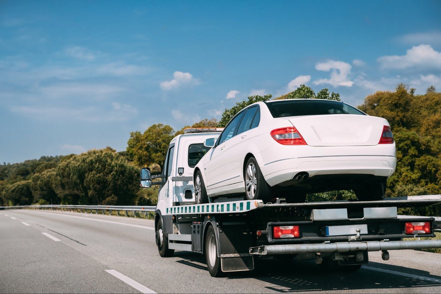 White sedan on a tow truck driving along a highway under a blue sky