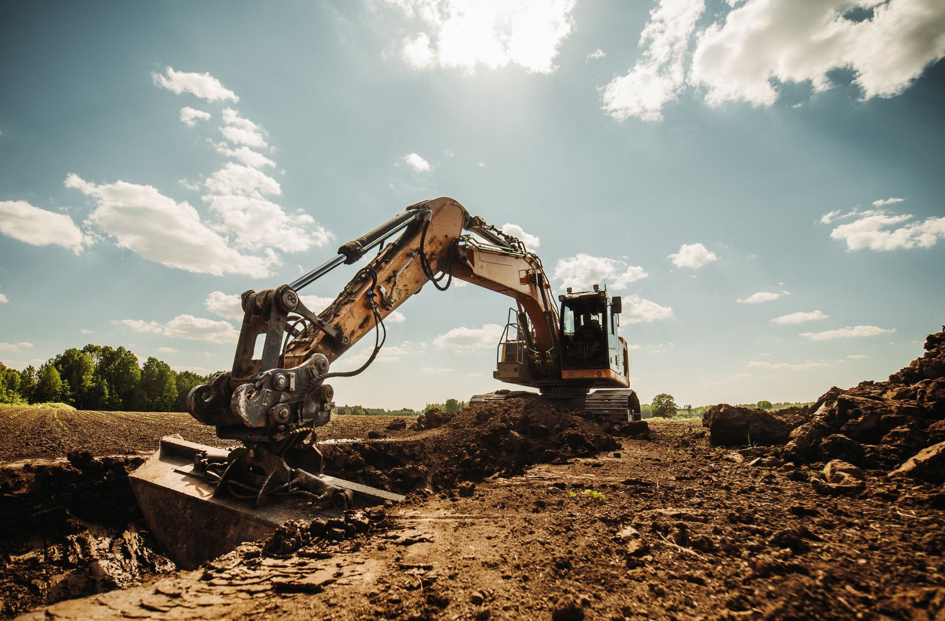 Excavator digging into dirt at an outdoor construction site under a bright blue sky Excavator digging into dirt at an outdoor construction site under a bright blue sky