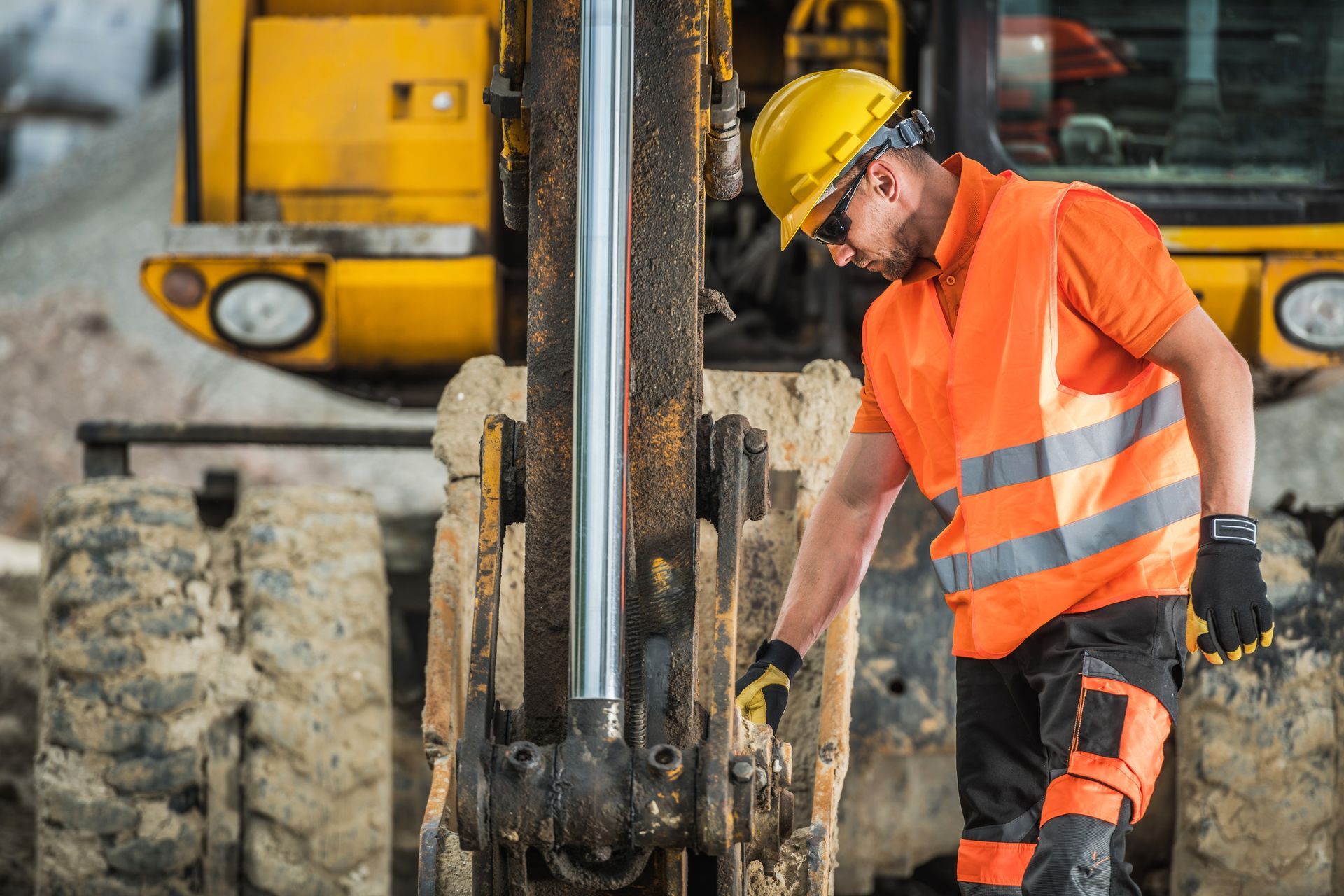 Construction worker in orange safety gear and hard hat inspecting drilling equipment at a work site