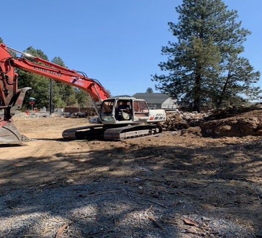 Skid steer and excavator clear land during early residential site prep near a suburban home. Skid steer and excavator clear land during early residential site prep near a suburban home.