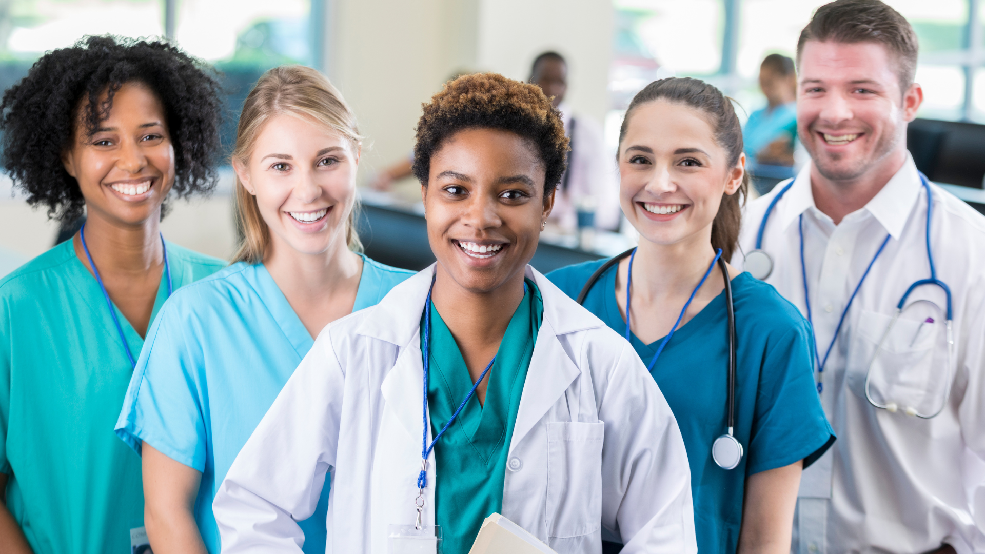 Group of smiling medical staff in white coats and scrubs standing together in a clinic