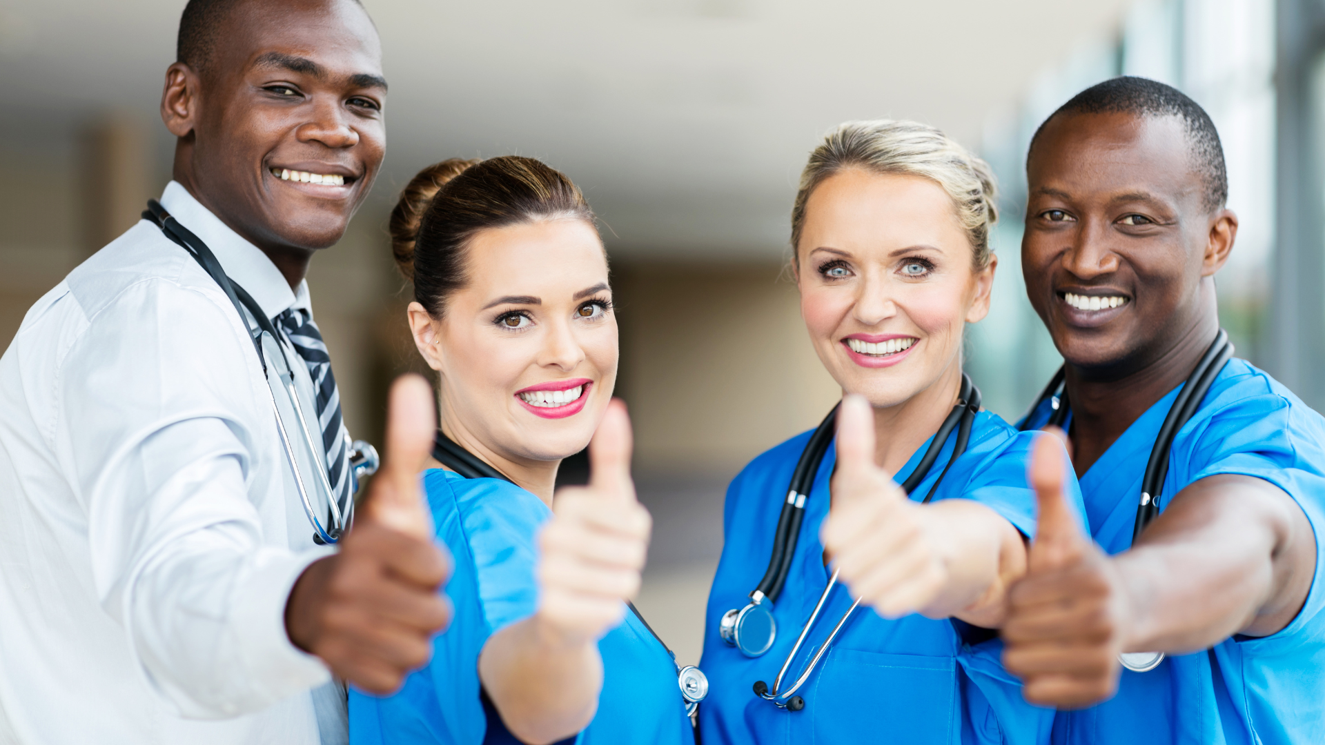 Smiling healthcare team in blue scrubs and a white coat giving thumbs up to the camera