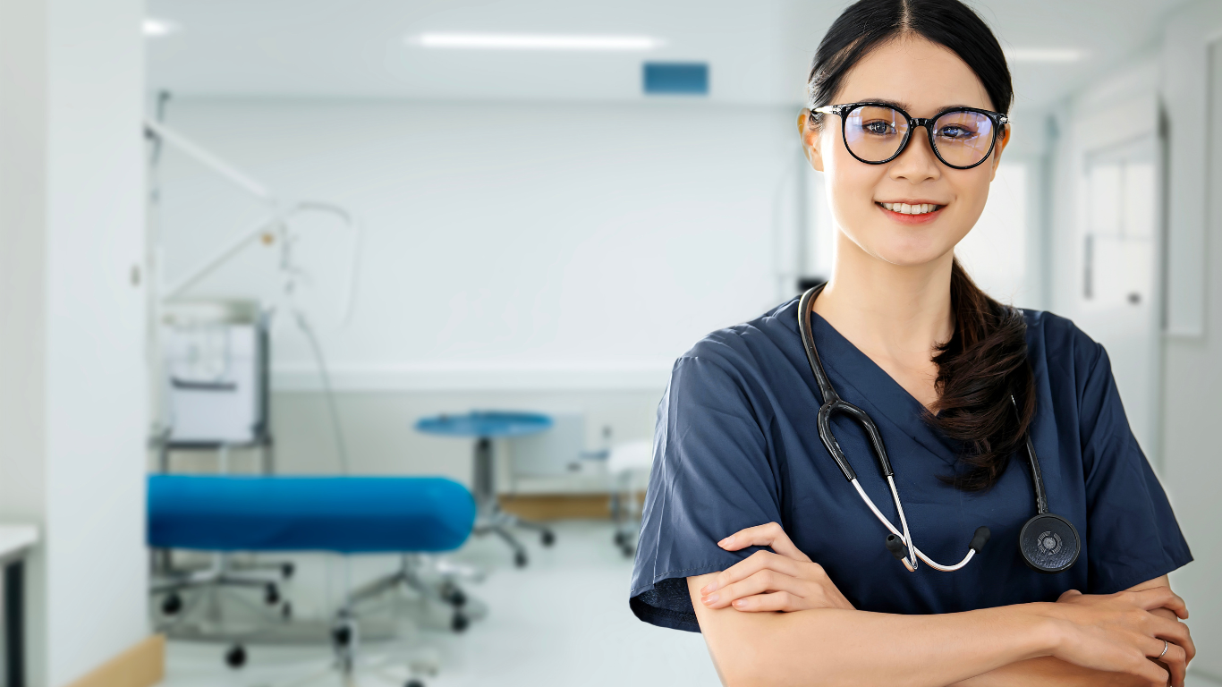 Smiling doctor in glasses and scrubs standing in a bright medical exam room