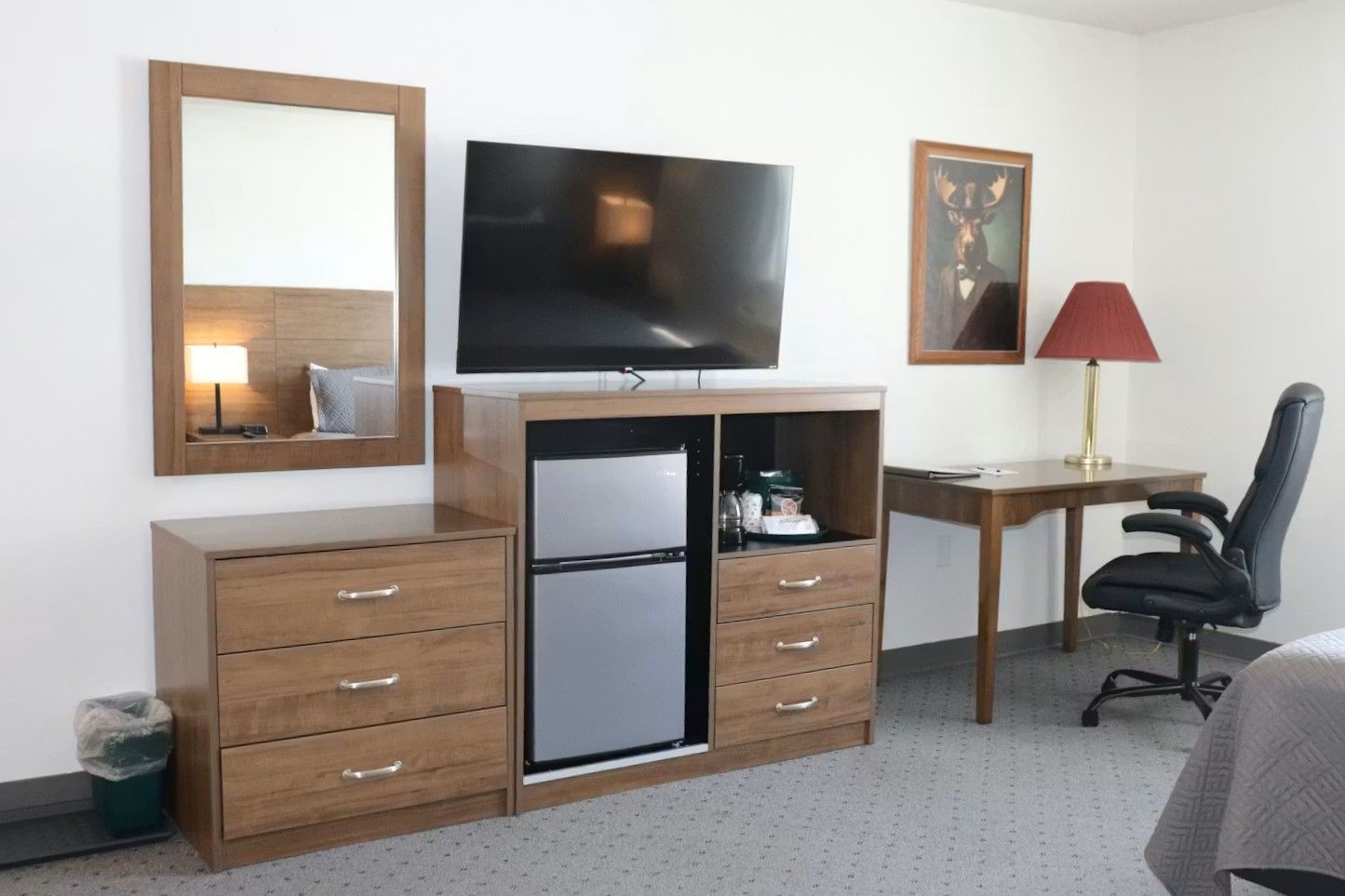 Hotel room with TV, dresser, mini-fridge, desk, mirror, and artwork.