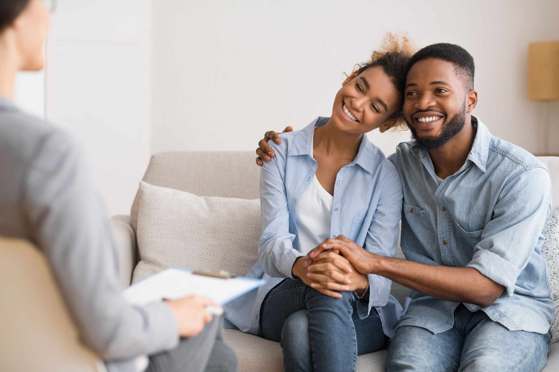 Couple smiling, holding hands, sitting on a sofa during couples therapy session. Couple smiling, holding hands, sitting on a sofa during couples therapy session.