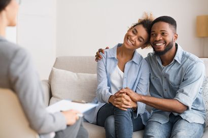 Couple smiling, holding hands, sitting on a sofa during couples therapy session. Couple smiling, holding hands, sitting on a sofa during couples therapy session.