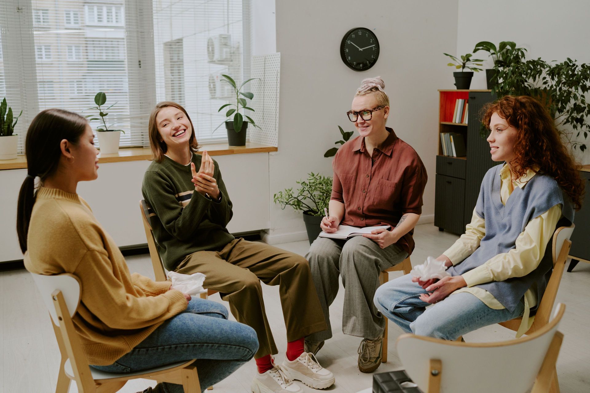 Four people seated in chairs, laughing and talking in a circle. Four people seated in chairs, laughing and talking in a circle.