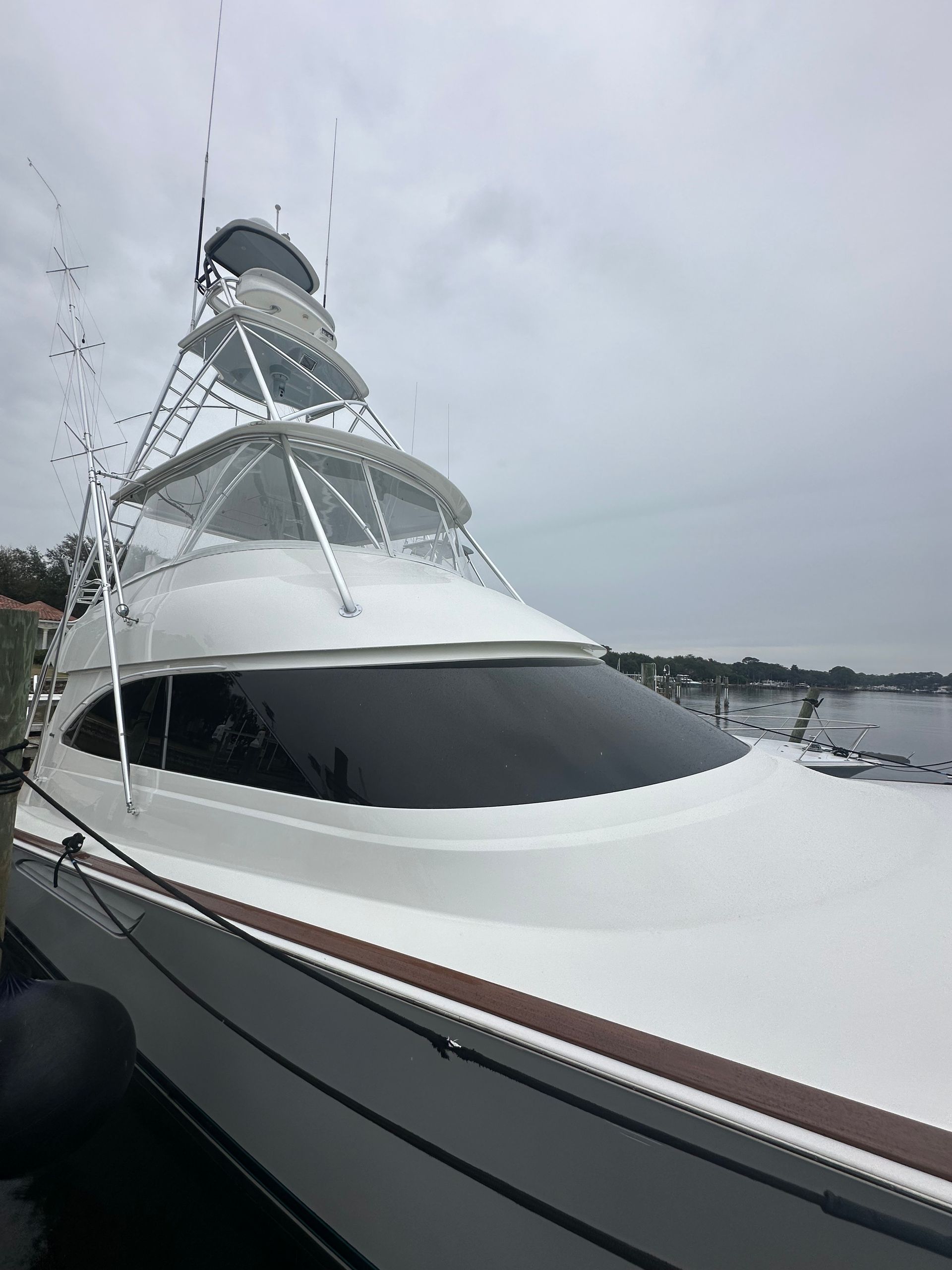 White yacht docked in harbor with tower, dark windows, and cloudy sky.