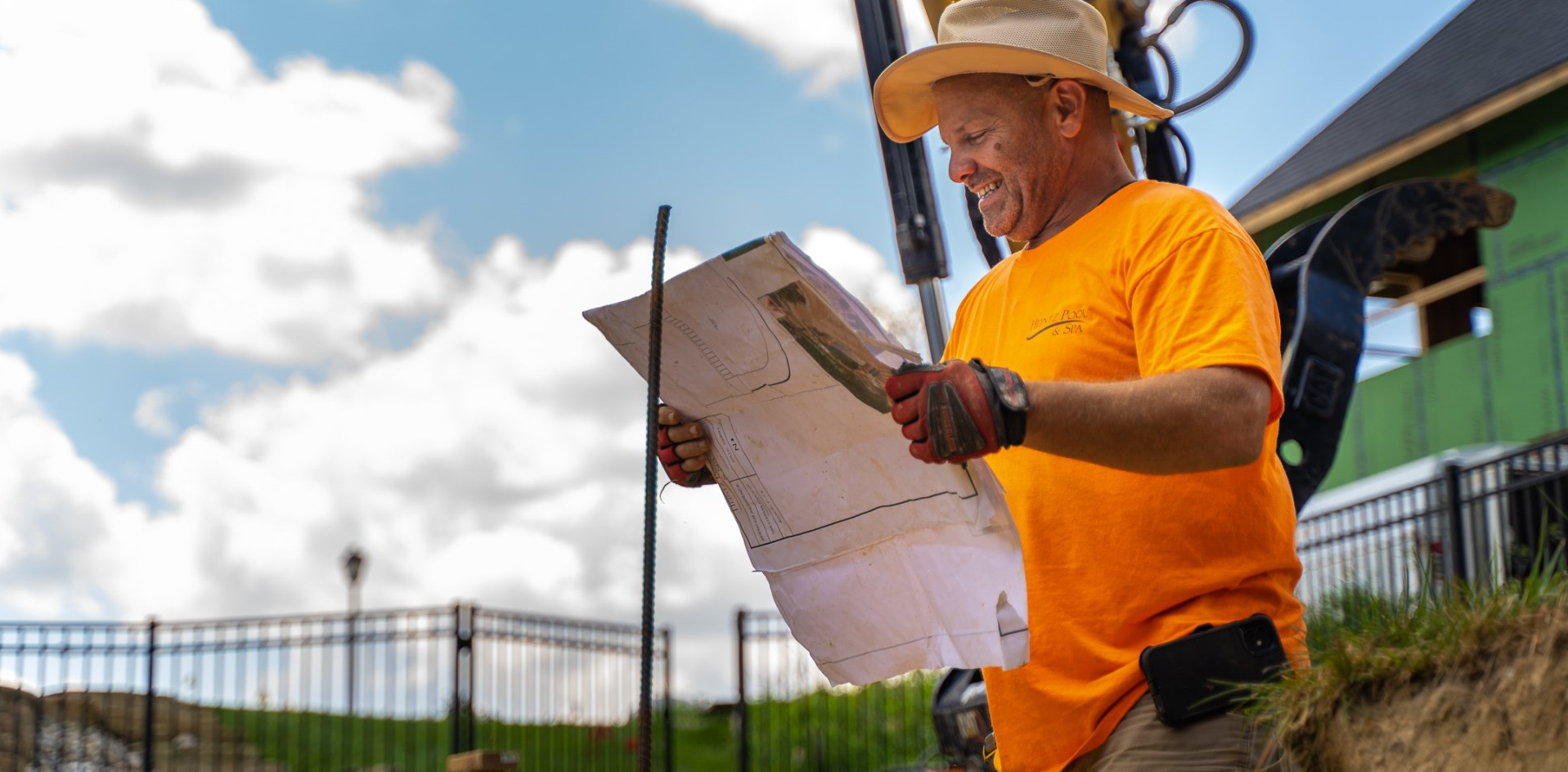 Contractor in an orange Heintz Pool & Spa uniform happily working while holding a pool blueprint