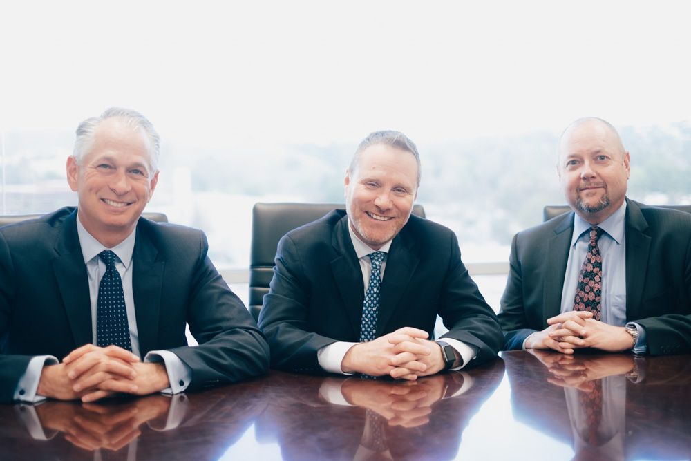 three men in suits and ties are sitting at a table with their hands folded