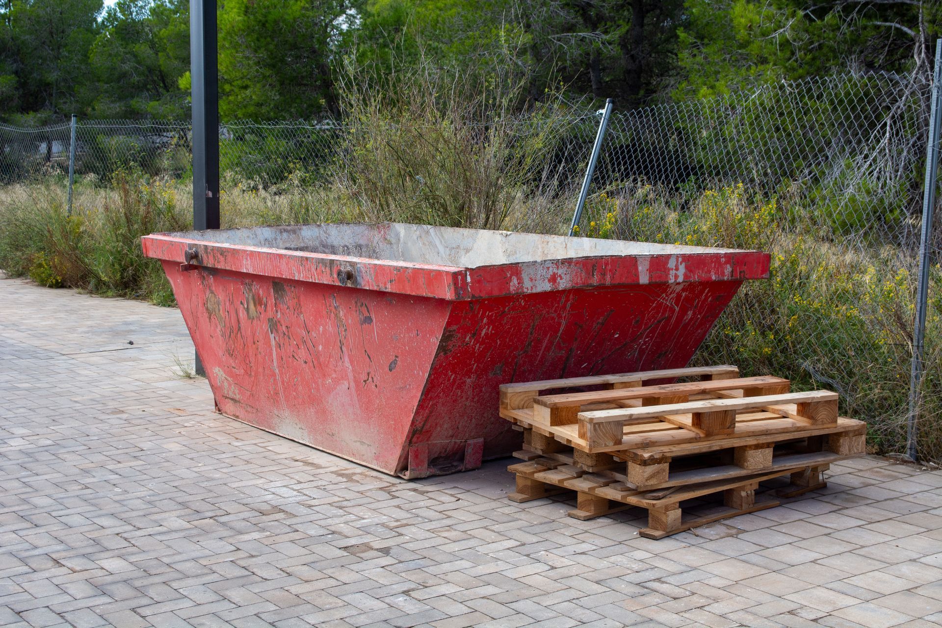 Dumpster rental featuring a red construction dumpster, highlighting stacked wooden pallets outdoors. Dumpster rental featuring a red construction dumpster, highlighting stacked wooden pallets outdoors.