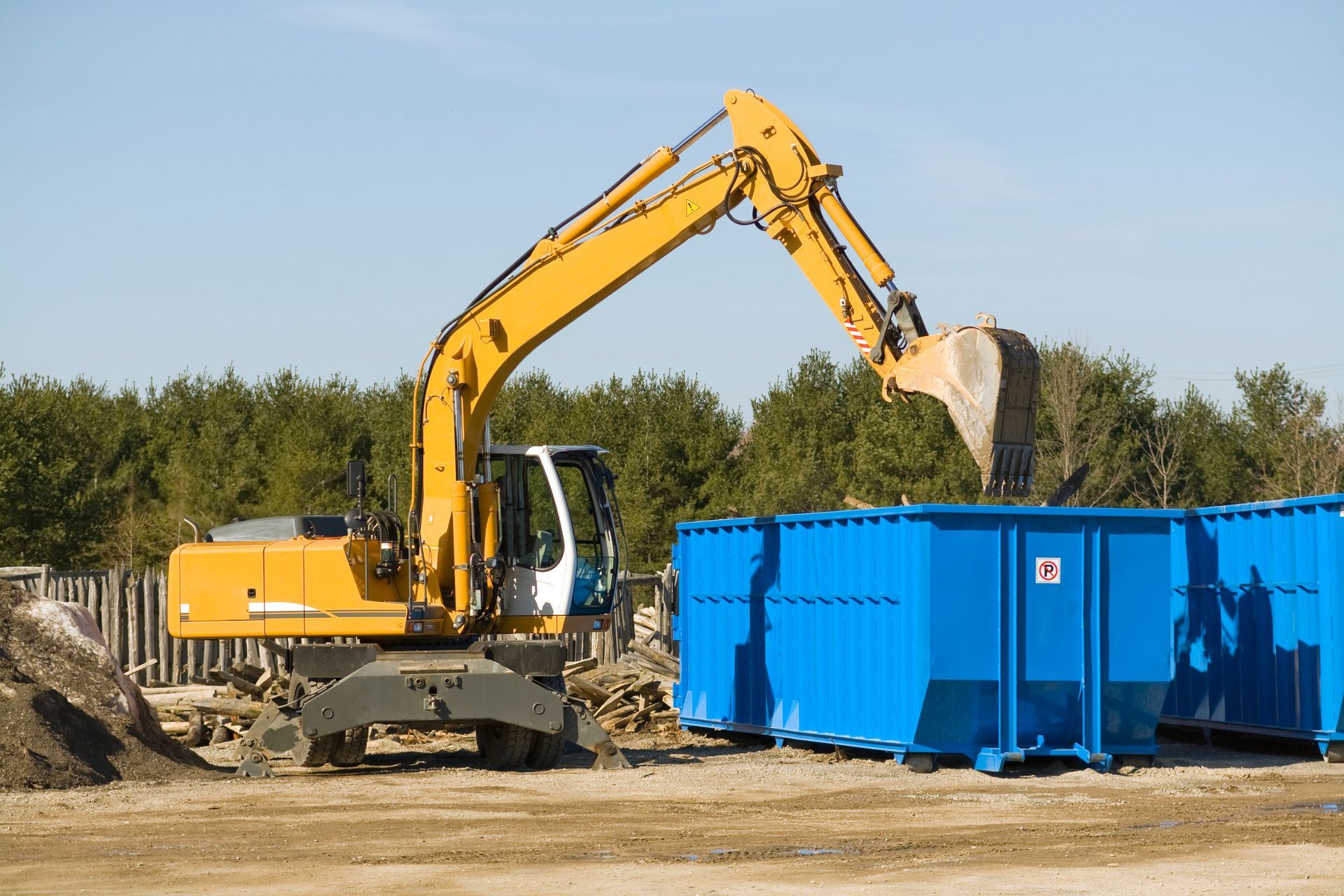 A demolition bulldozer taking debris to a blue dumpster in a construction site.