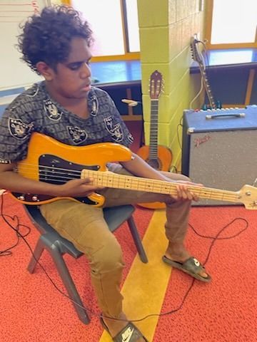 Person seated with an electric bass guitar in a music room, near an amplifier and mic stand.