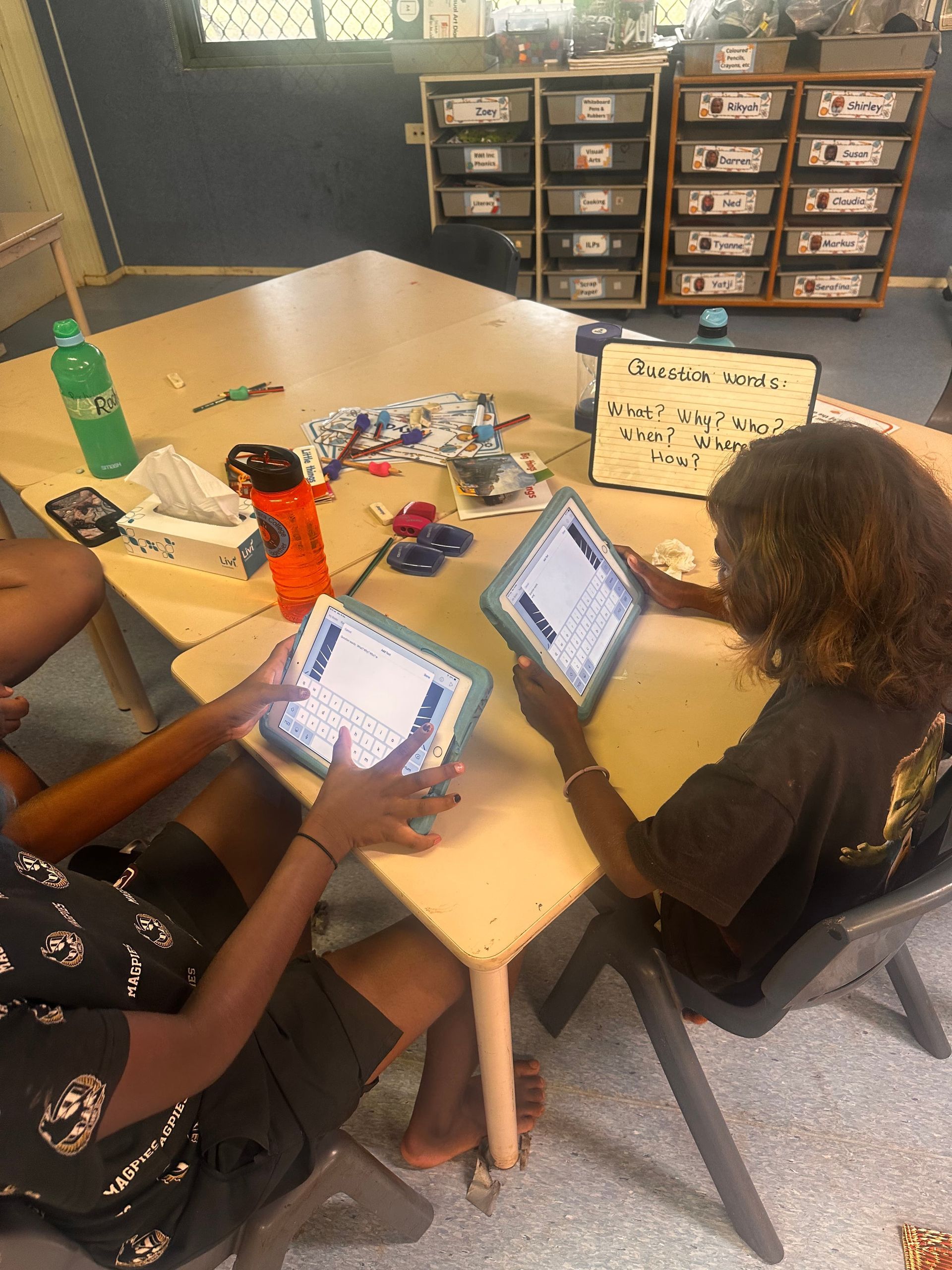 People at a table using tablets and craft supplies in a classroom setting