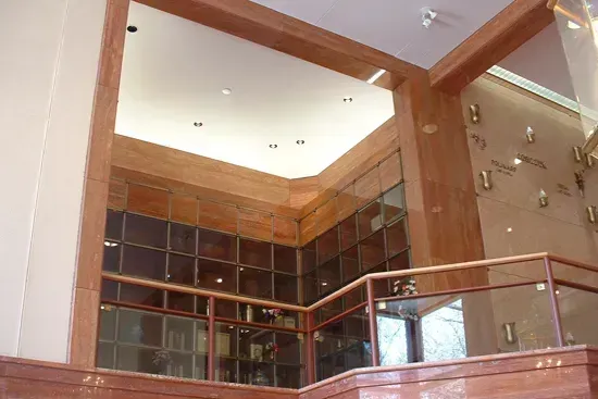Modern interior with wooden beams, glass railing, and dark shelving under a skylit ceiling