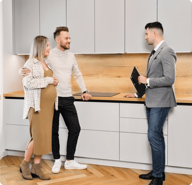 A couple and realtor in a modern kitchen. The woman is pregnant. The realtor holds a clipboard.