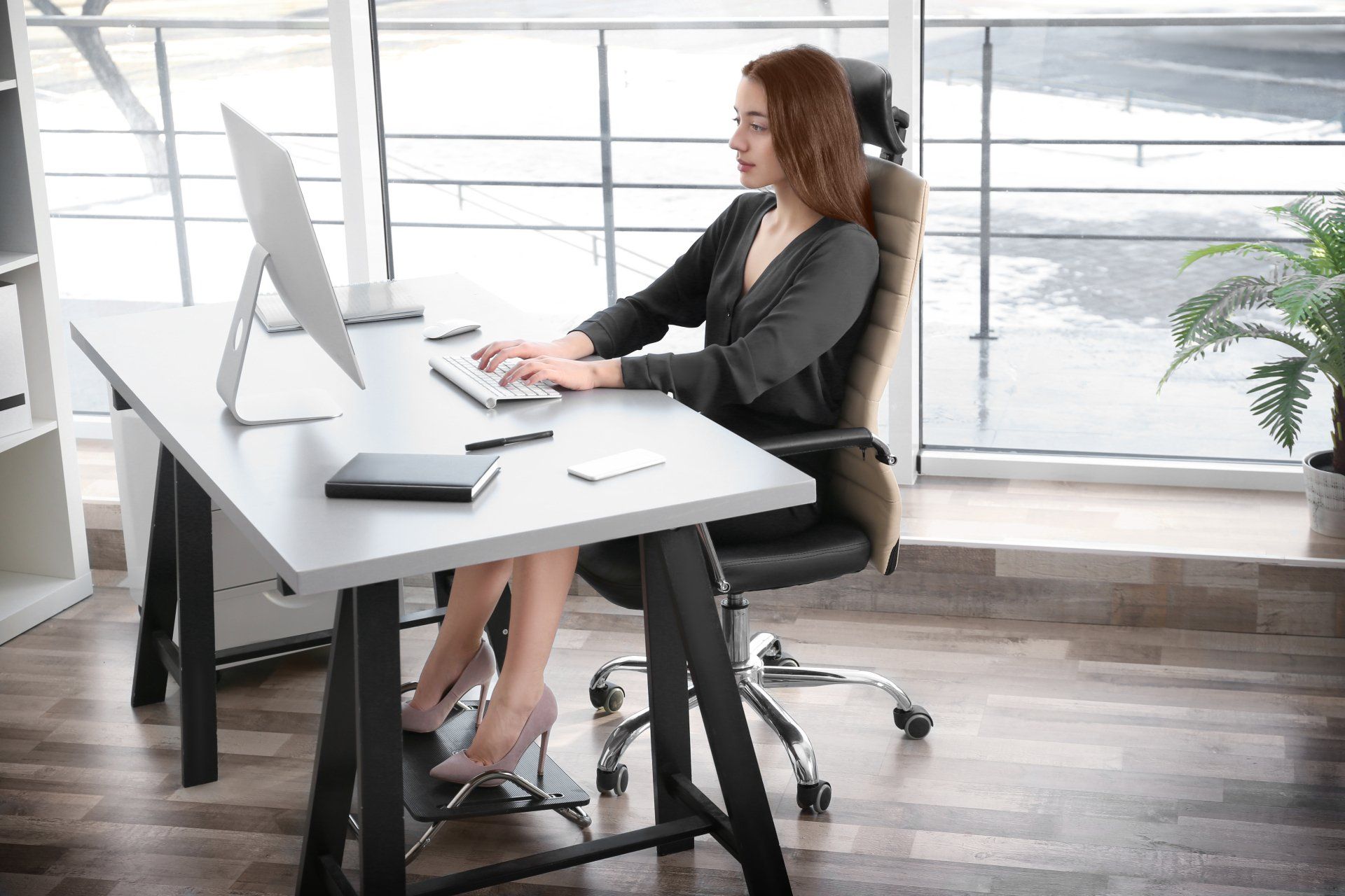 Woman typing at a modern desk in a bright office with large windows