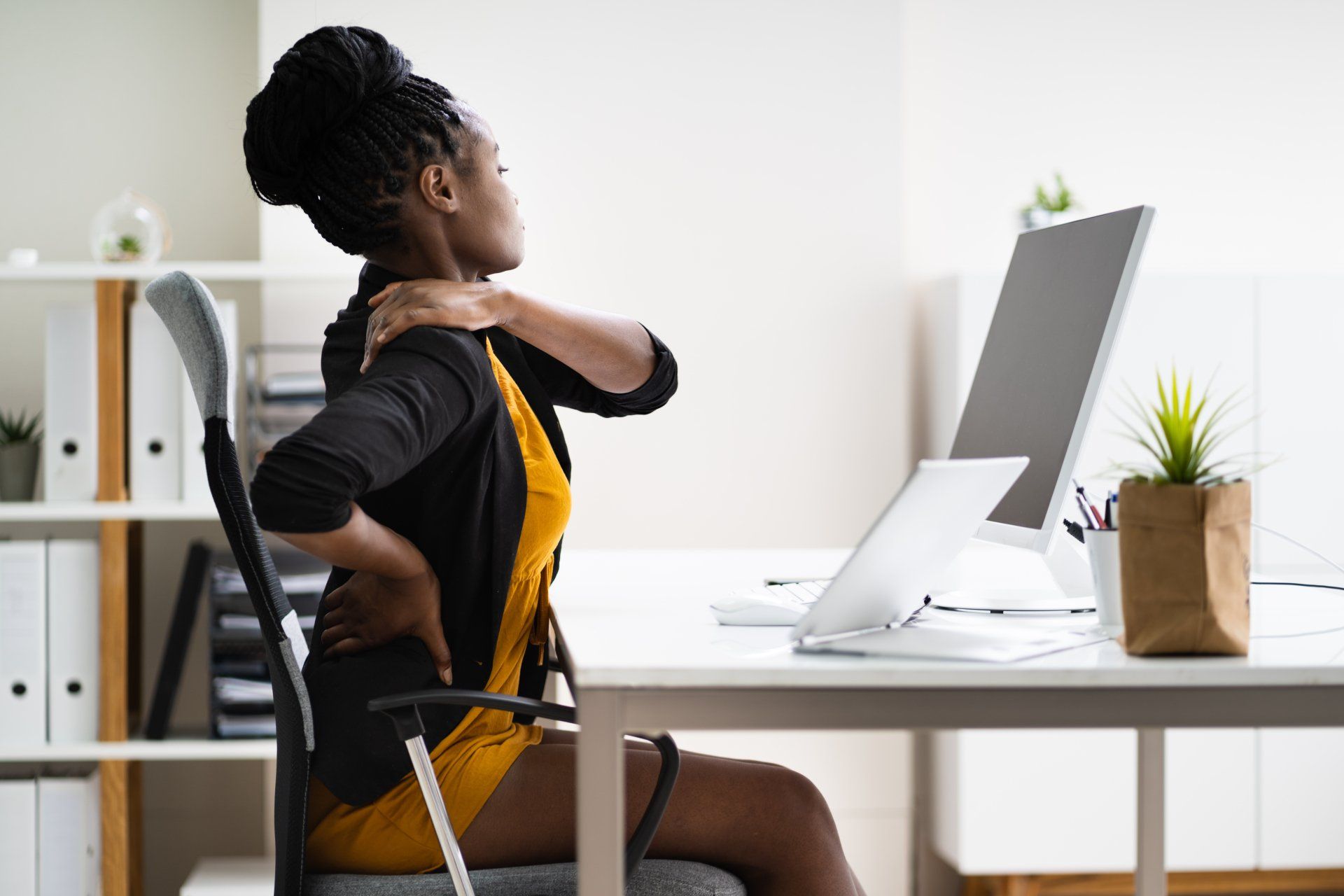 Une femme est assise à un bureau avec un ordinateur et étire son dos.
