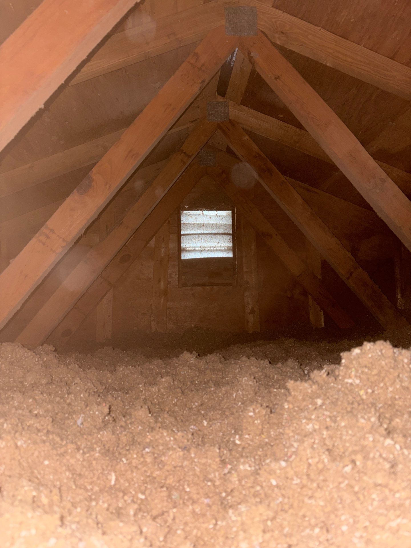 Attic with wooden beams and insulation, showing a small window at the far end.