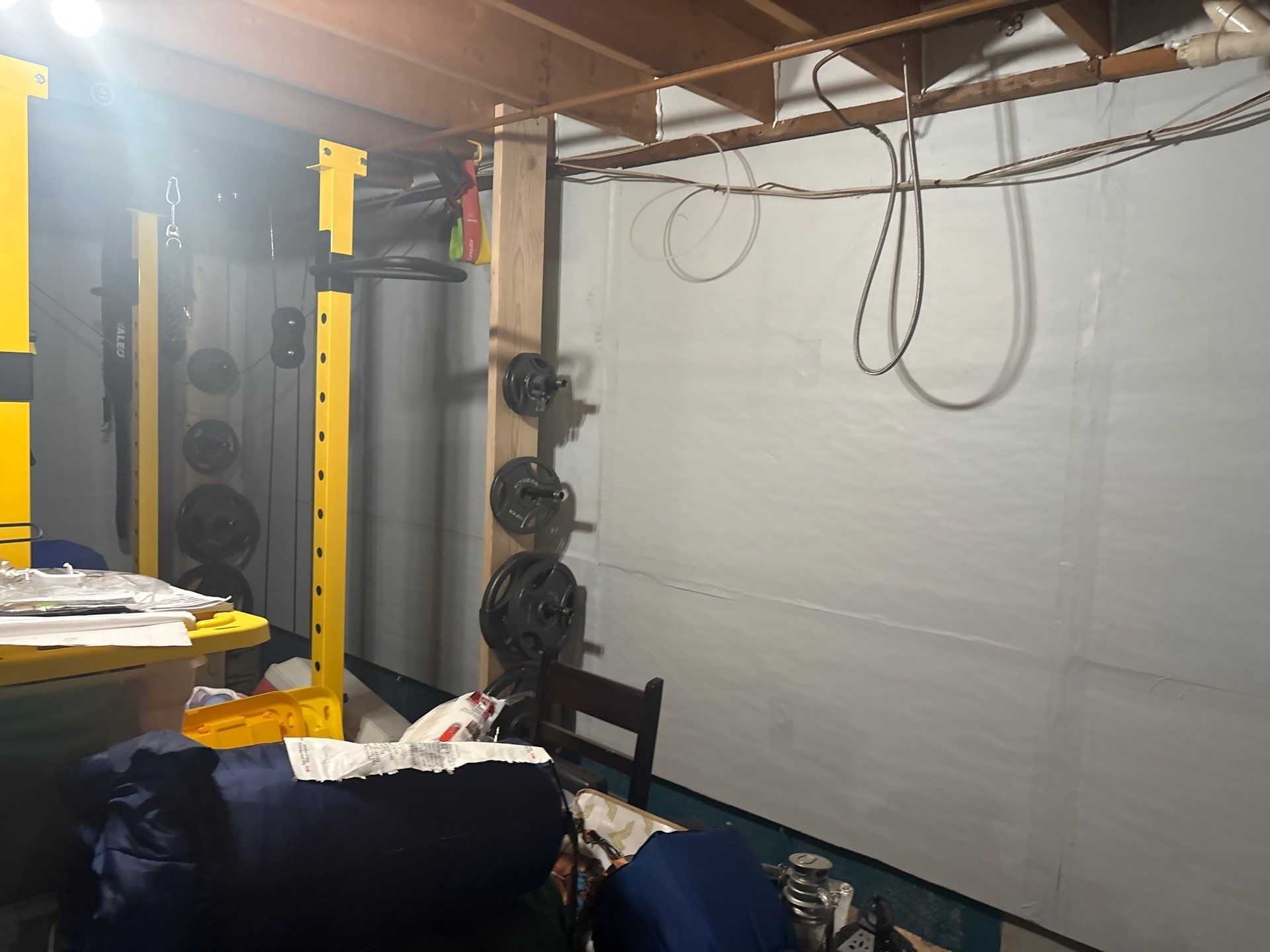 Indoor basement gym with yellow rack, weight plates, hanging cords, and white wall panels