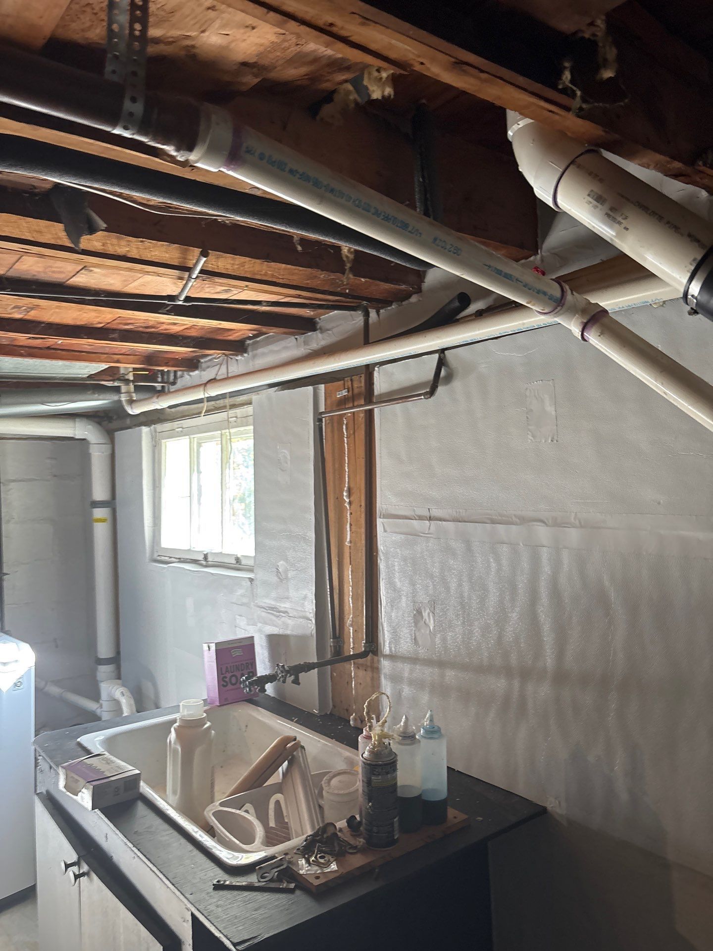 Partially renovated room with exposed ceiling beams, white walls, window, and workbench with tools and debris