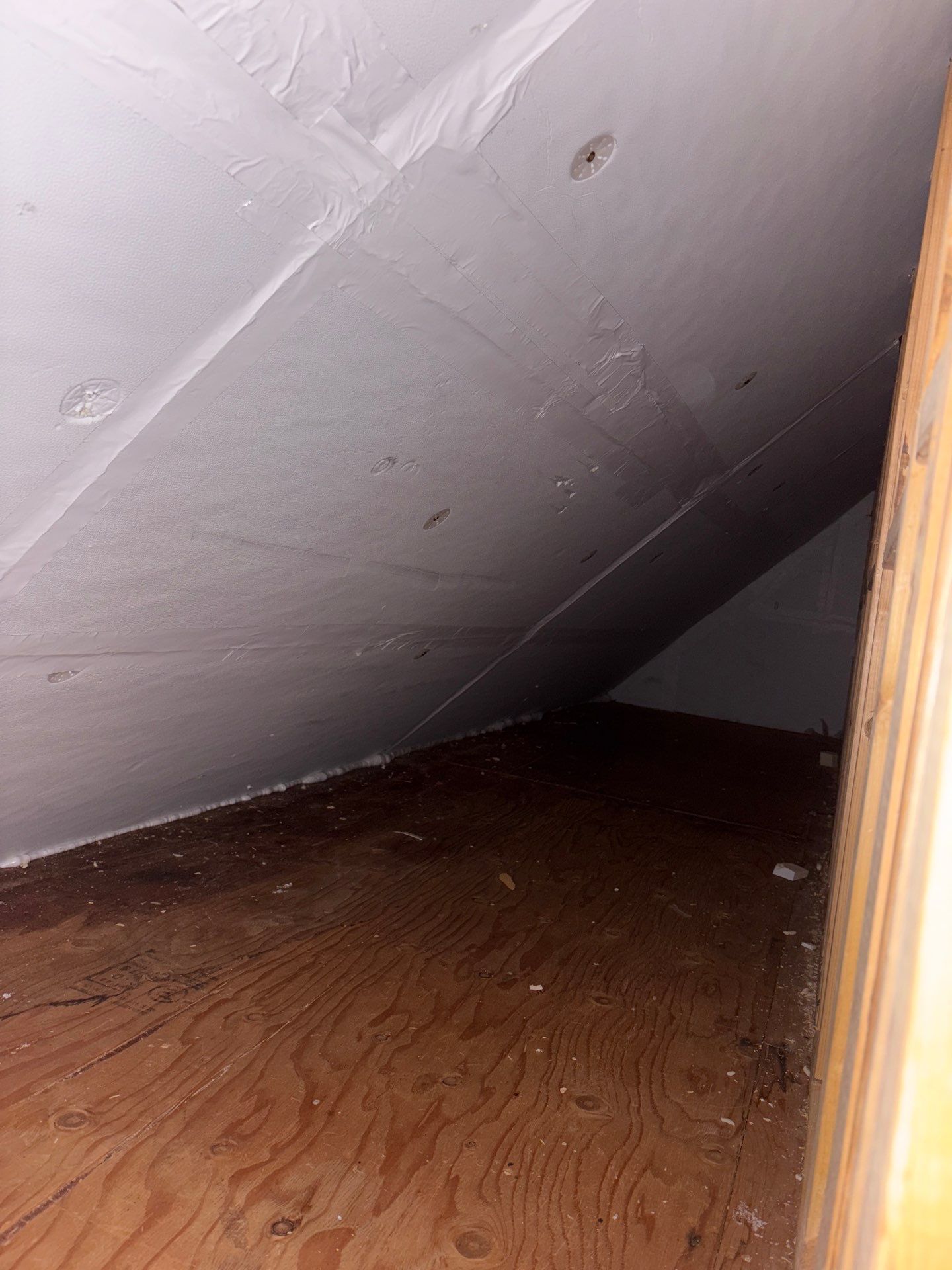 Empty attic crawlspace with slanted white wall and brown wooden floorboards