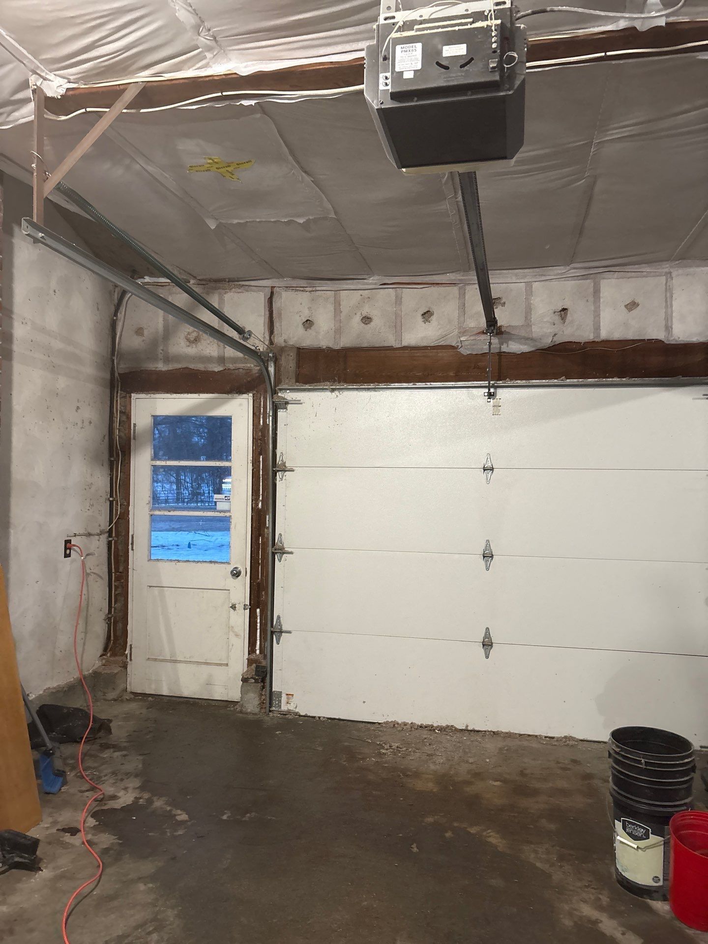 Garage interior with white overhead door, side entry, wet concrete floor, and a garage door opener overhead