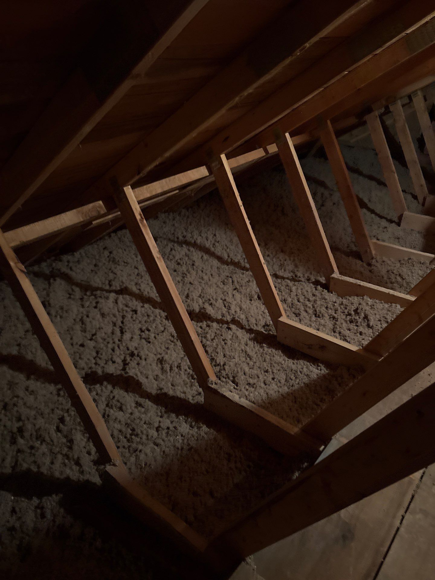 Wooden attic staircase with exposed beams and insulation in a dim interior