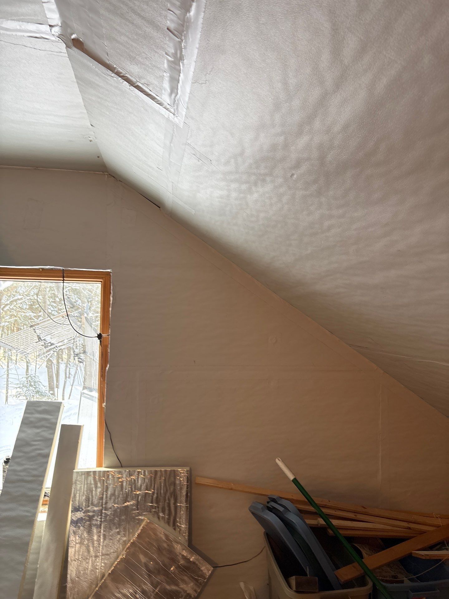 Attic interior with slanted white ceiling, window light, and stacked boards and tools on the floor