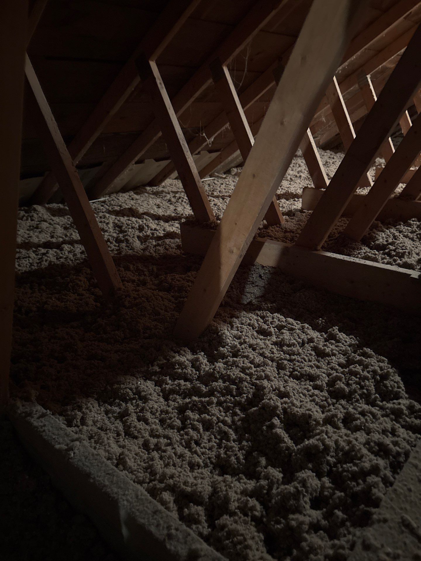 Attic roof interior with wooden beams and piles of insulation material on the floor