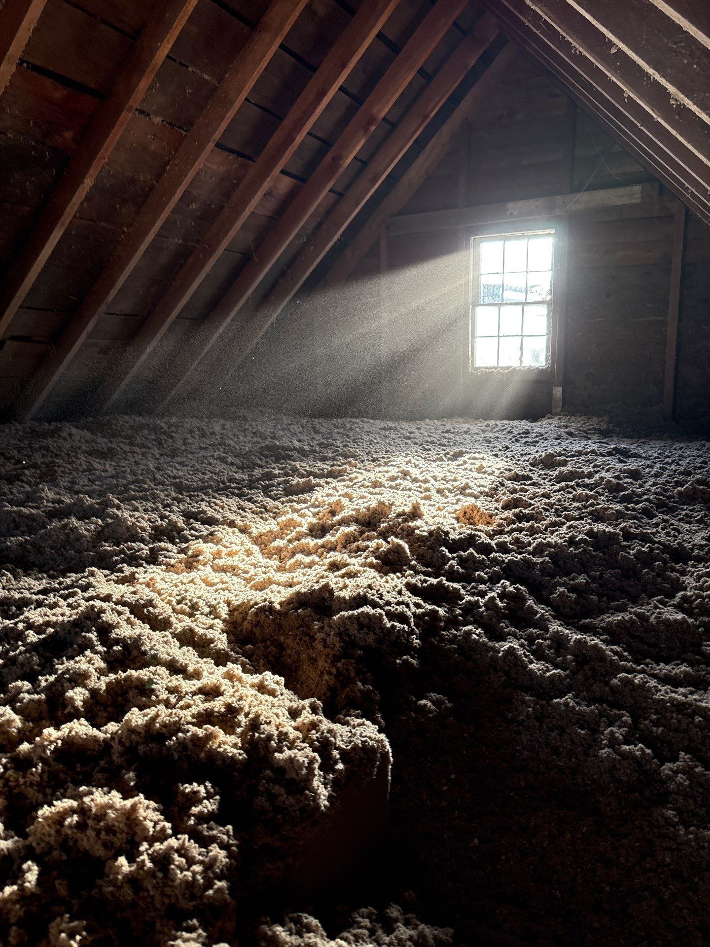 Sunlit attic with wooden beams and loose insulation piled on the floor