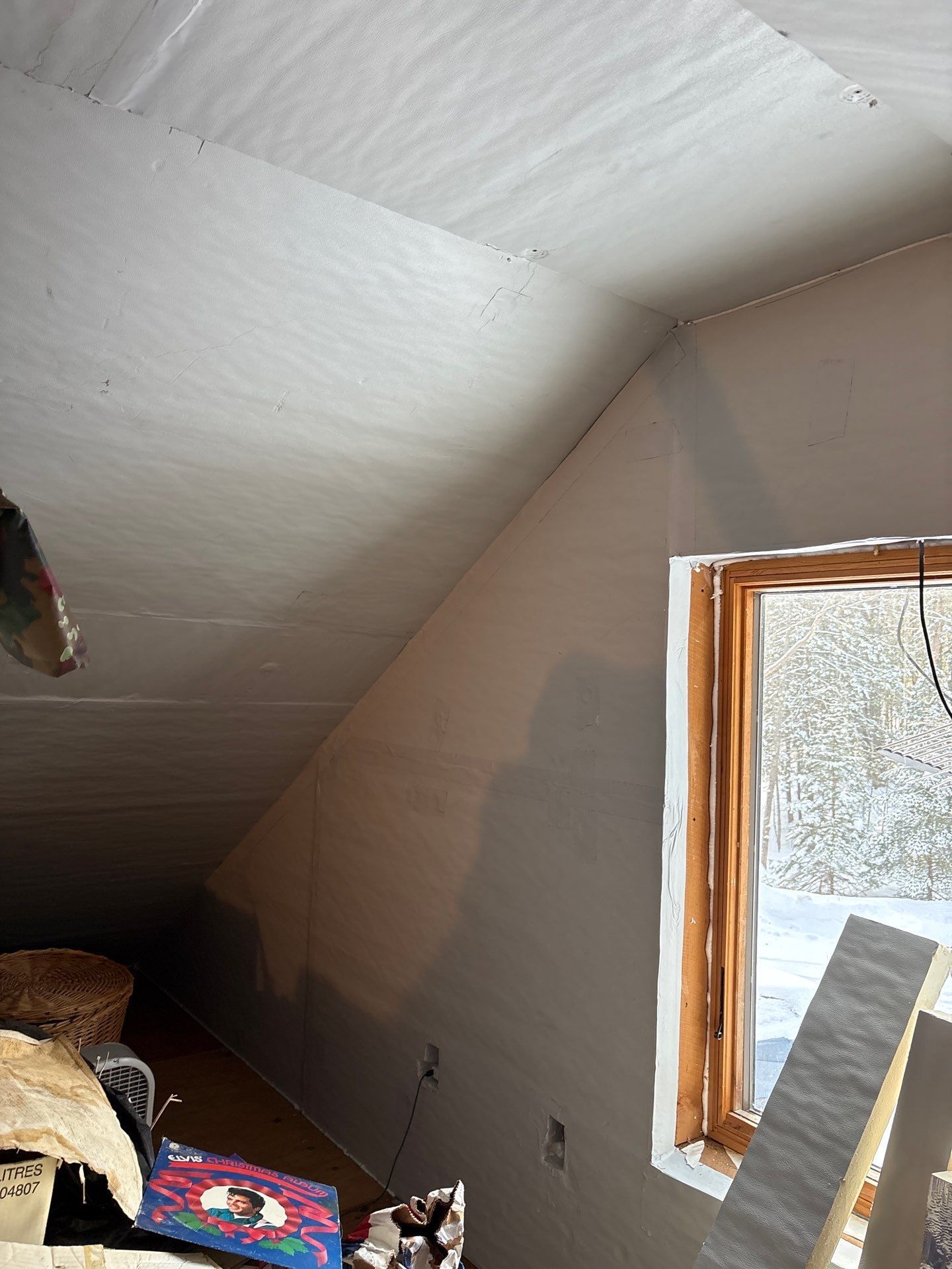 Slanted attic ceiling with a small window and a painted wall, with a bed corner and rug in the lower left.
